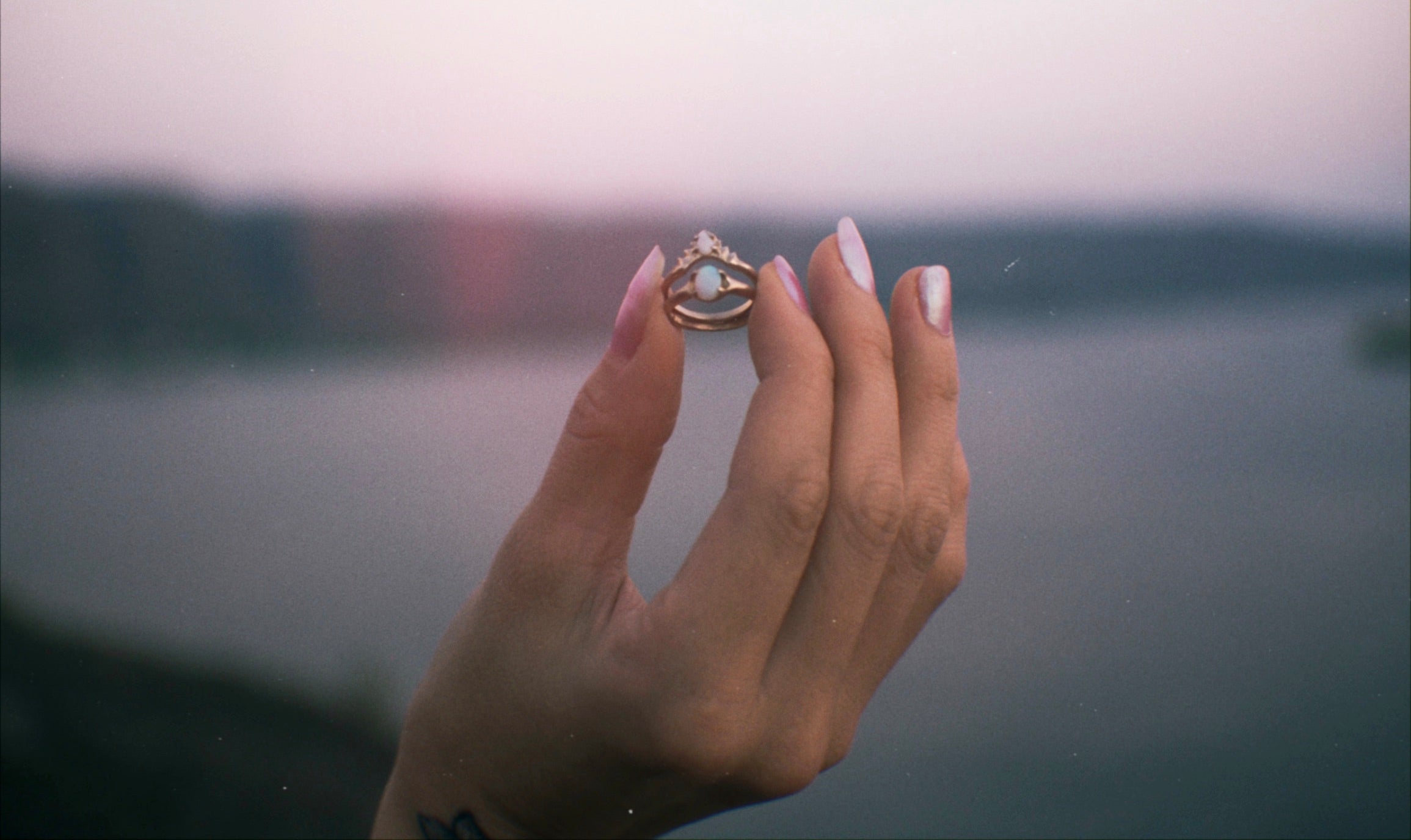 Ethical engagement rings set with sustainably sourced natural opal made by Iron Oxide Designs. The rings are being held by a model with painted nails against a background of the Columbia River Gorge.