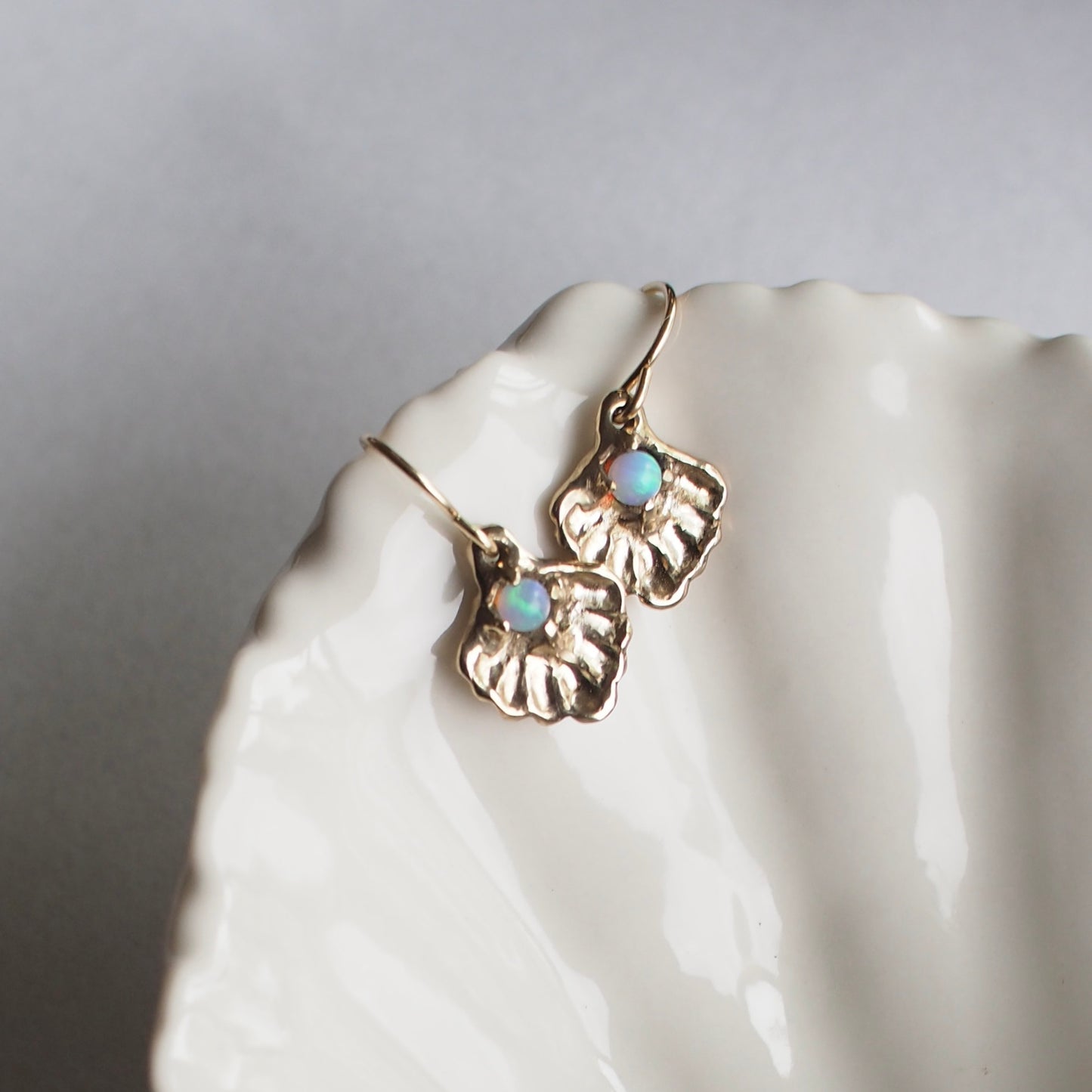 Oyster shell earrings containing a small opal "pearl", cast in gold tone bronze by Iron Oxide Designs