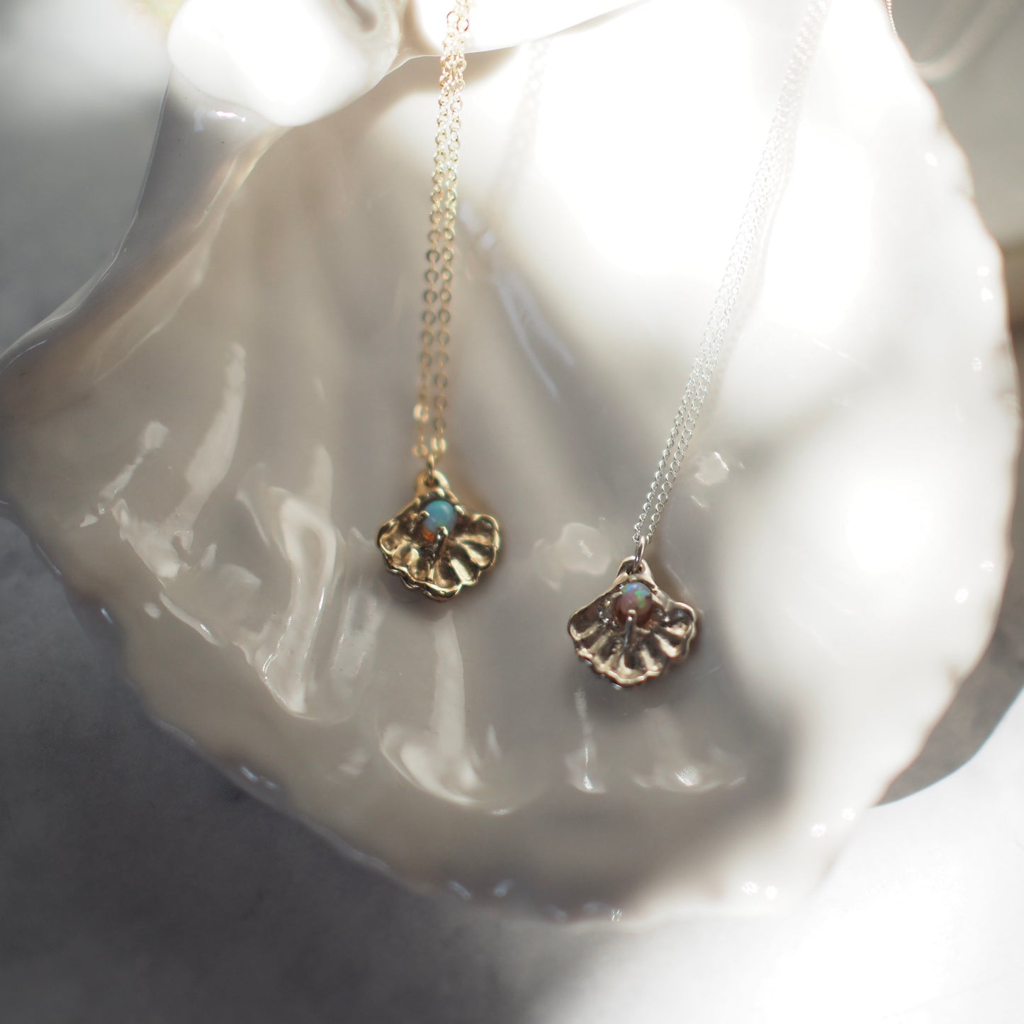 Close up of a gold tone and silver Seashell necklace containing a tiny opal in place of a pearl, handmade by Iron Oxide Designs