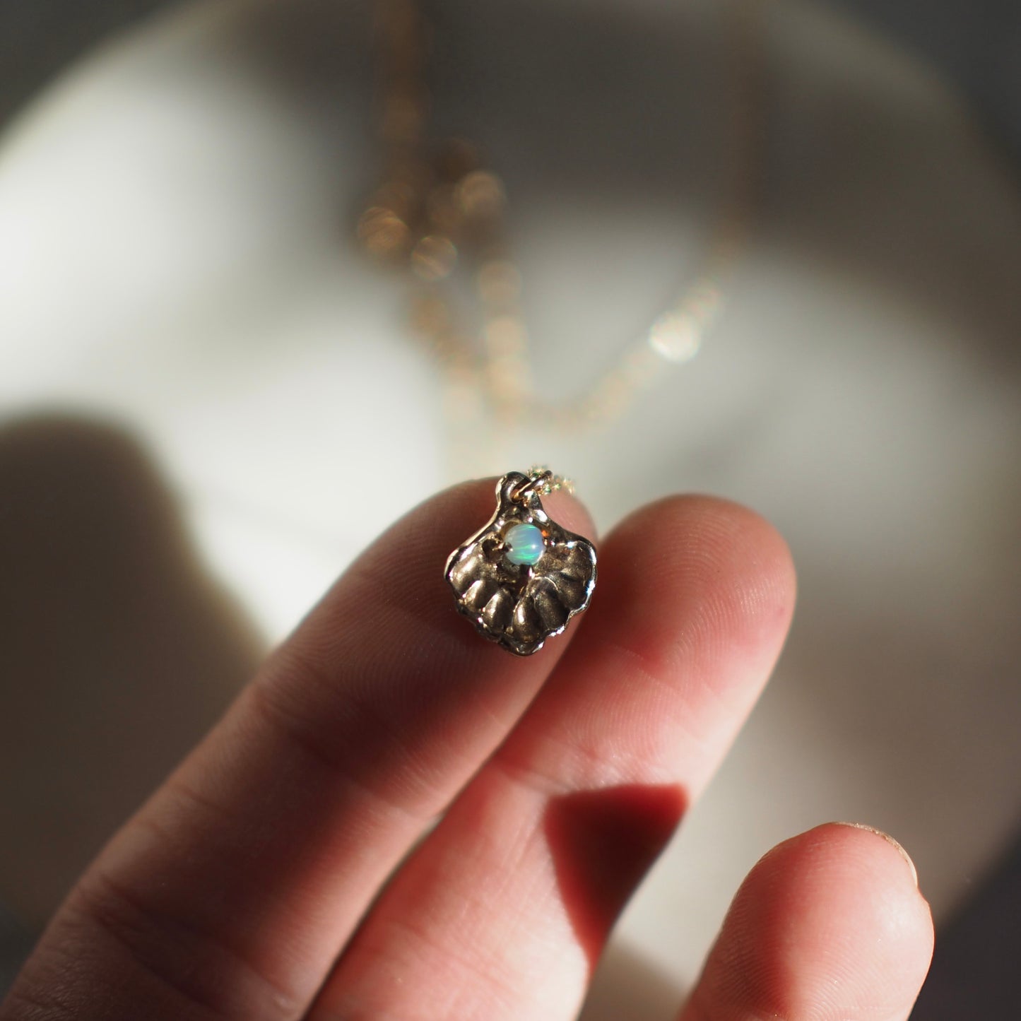 Close up of a gold tone Seashell necklace containing a tiny opal in place of a pearl, handmade by Iron Oxide Designs