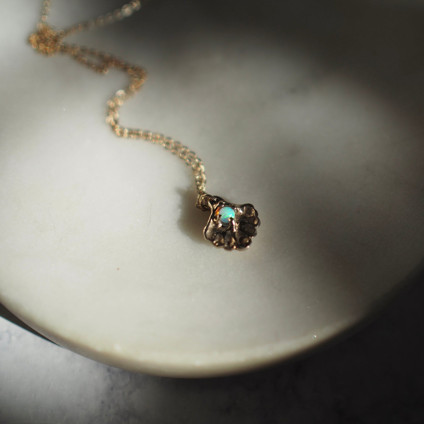 Close up of a gold tone Seashell necklace containing a tiny opal in place of a pearl, handmade by Iron Oxide Designs