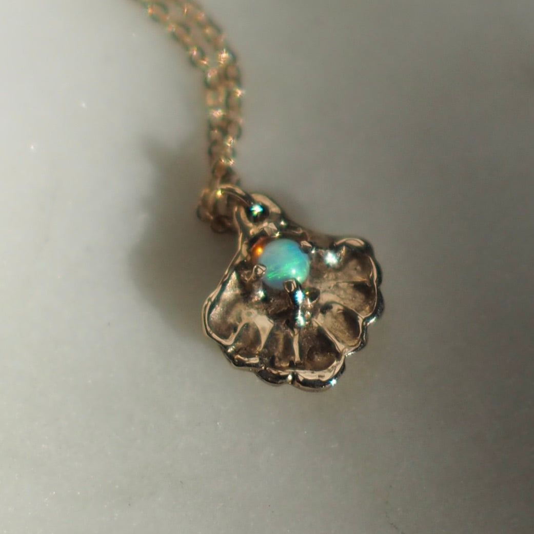 Close up of a gold tone Seashell necklace containing a tiny opal in place of a pearl, handmade by Iron Oxide Designs