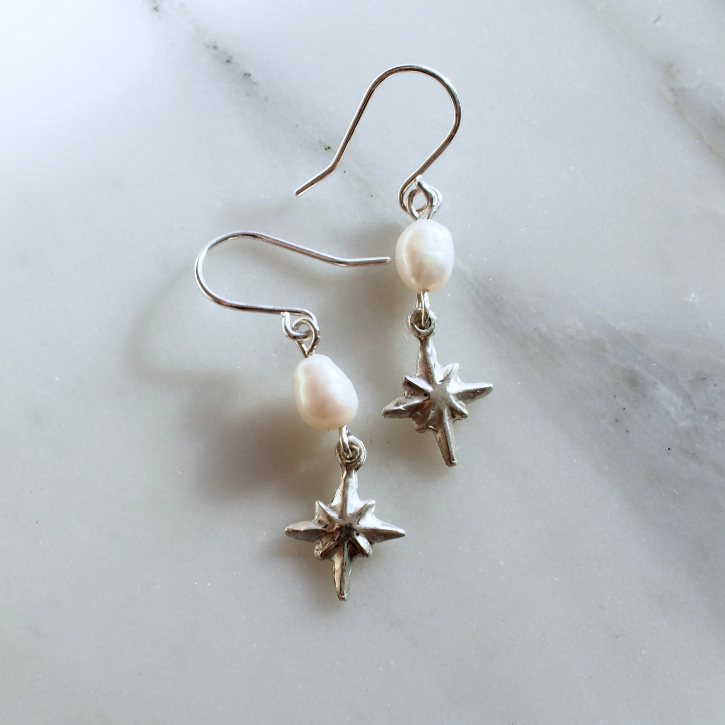 Dainty pearl and star earrings, featuring a 7mm oval shaped pearl with a tiny silver star hanging below it.