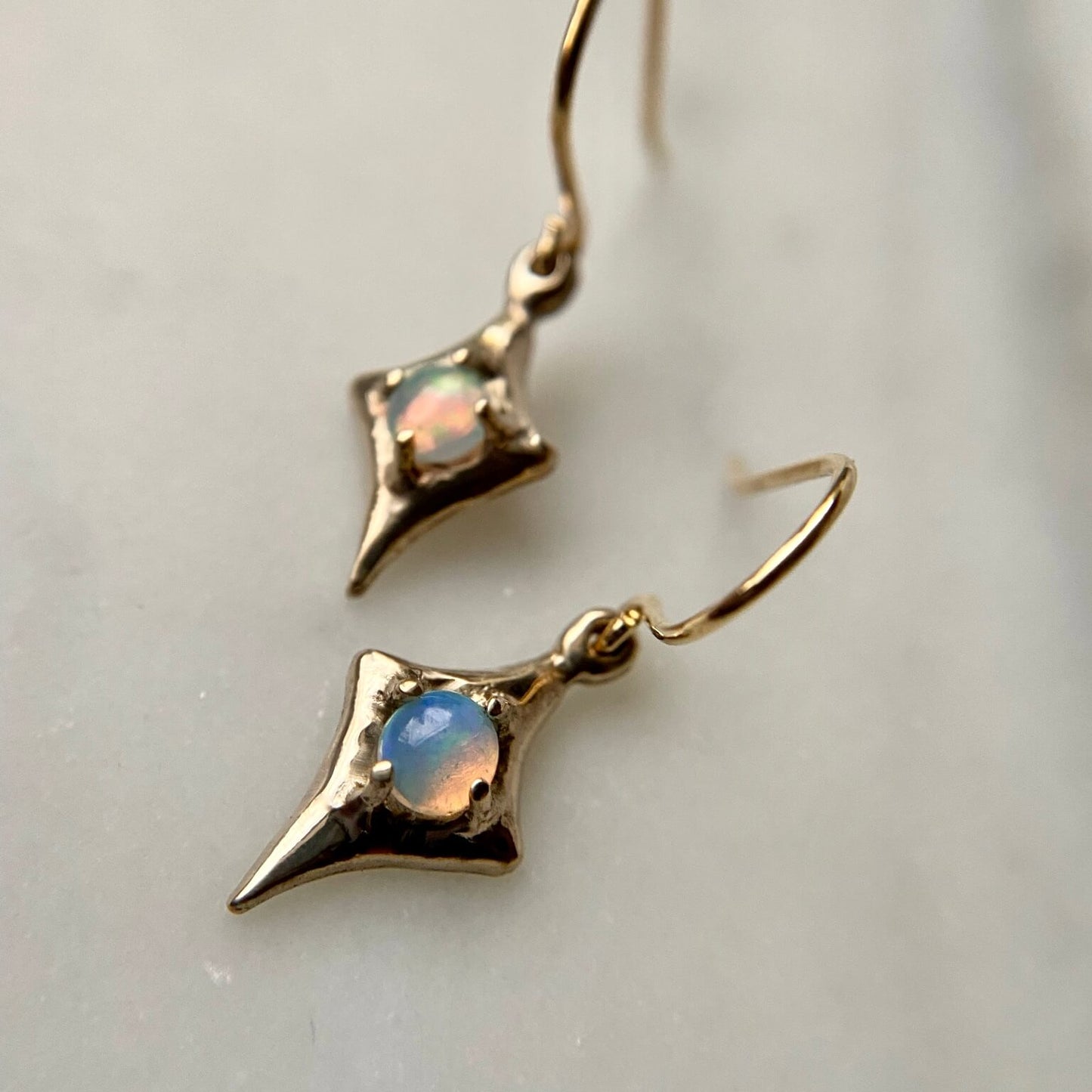 Close up of Four point star earrings from Iron Oxide Designs set with 4mm natural opals