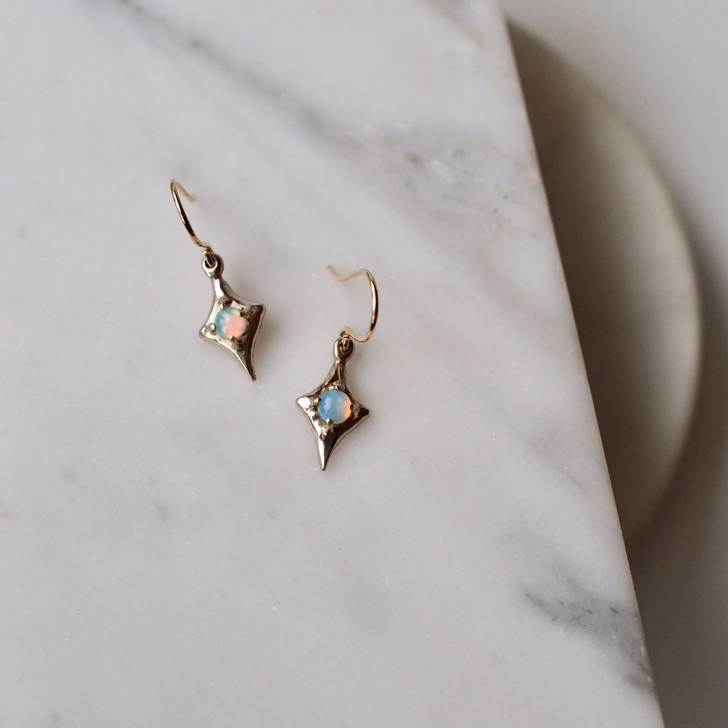 Four point star earrings from Iron Oxide designs set with 4mm natural opals on a marble backdrop
