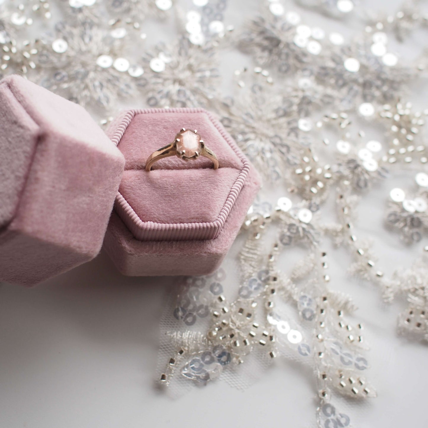 Peach Sunstone Engagement ring held in a pink velvet gift box on top of bridal lace
