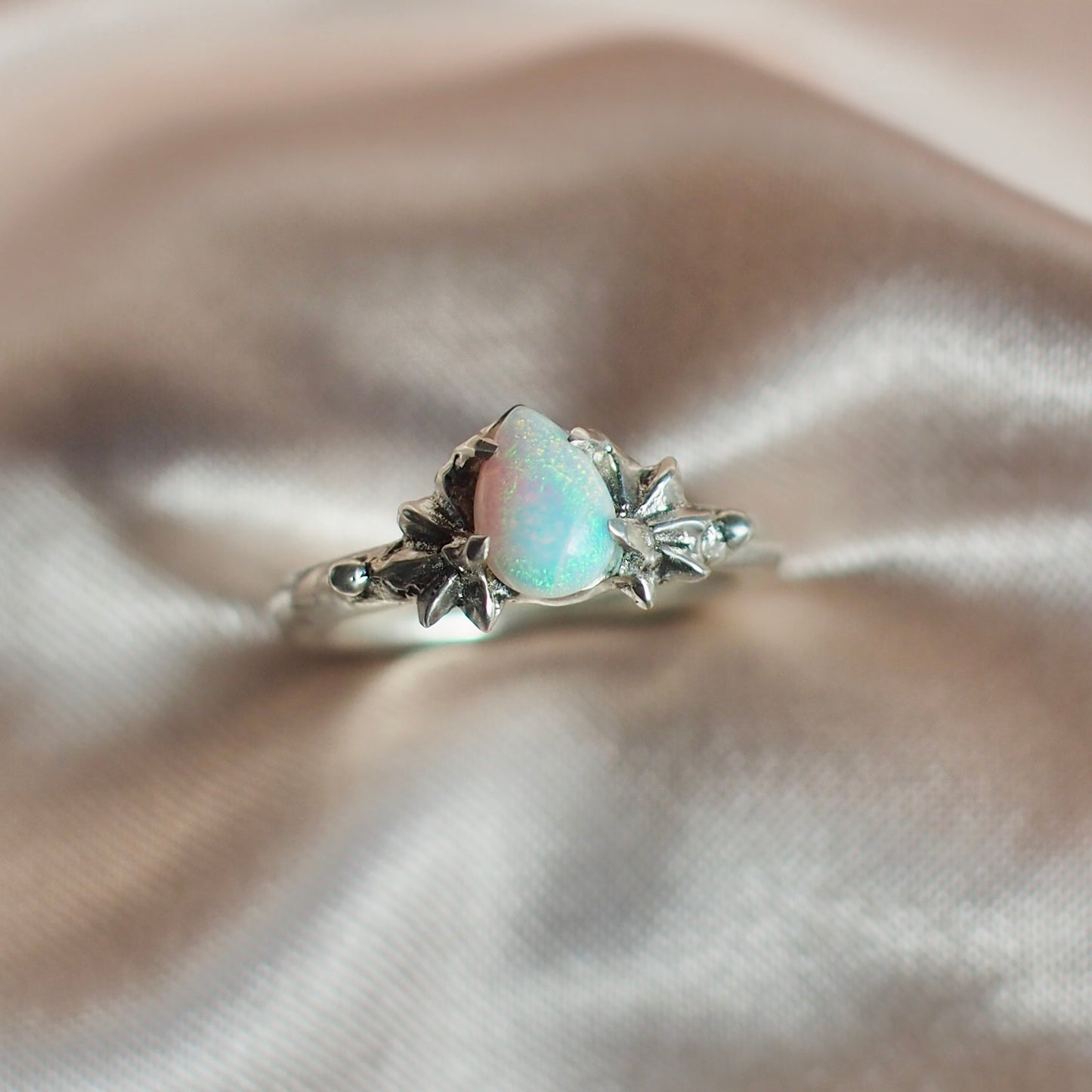 Close up of Teardrop shaped lab grown opal set between two star setting in sterling silver by Iron Oxide Designs
