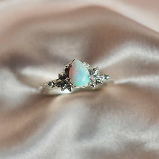 Close up of Teardrop shaped lab grown opal set between two star setting in sterling silver by Iron Oxide Designs