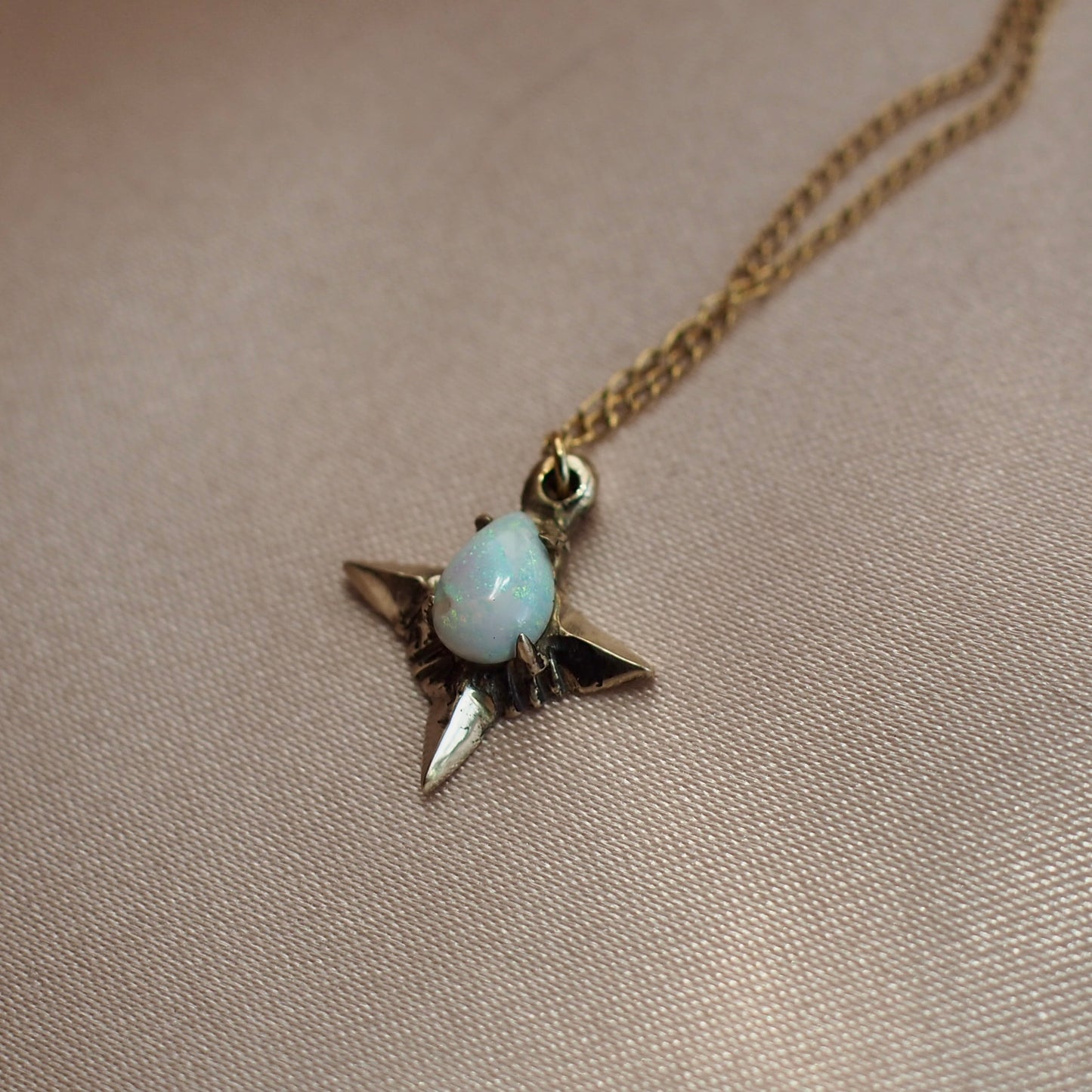 Close up of Teardrop shaped lab grown opal set in a four point star in gold tone bronze handmade by Iron Oxide Designs