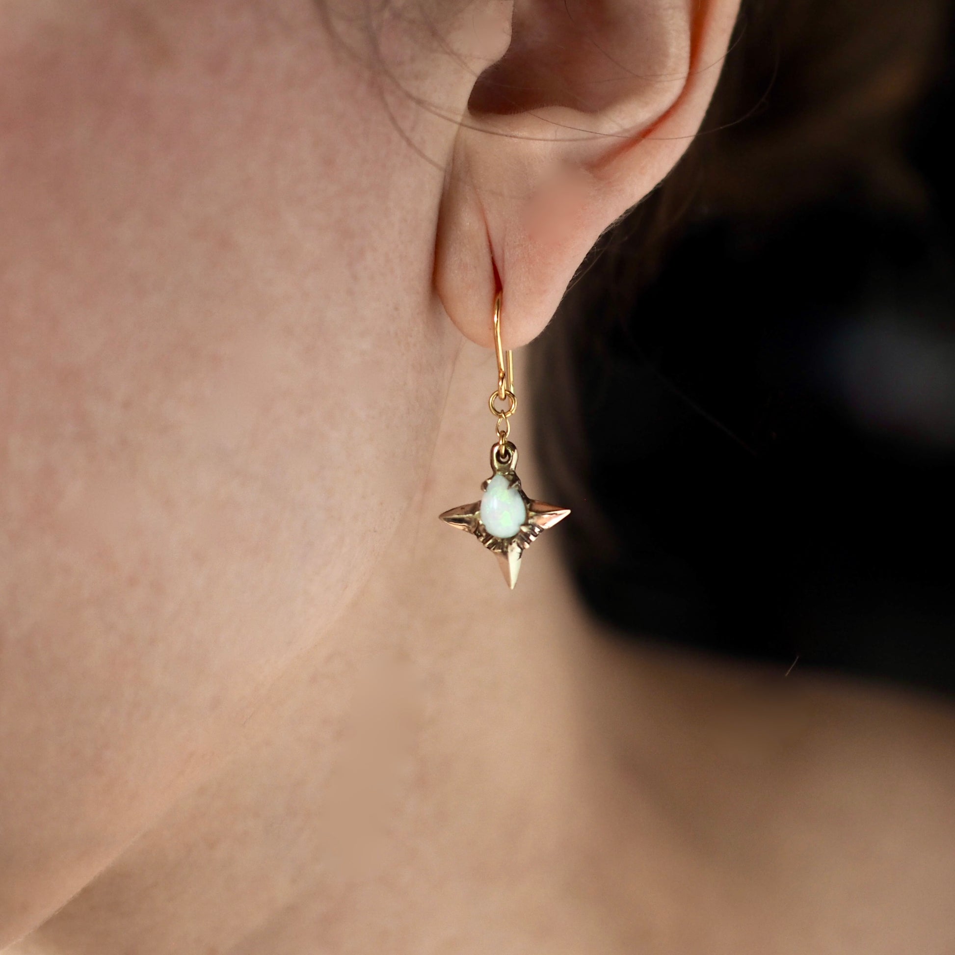 Teardrop shaped lab grown opal set in 4 point star setting in gold tone bronze handmade by Iron Oxide Designs on a model