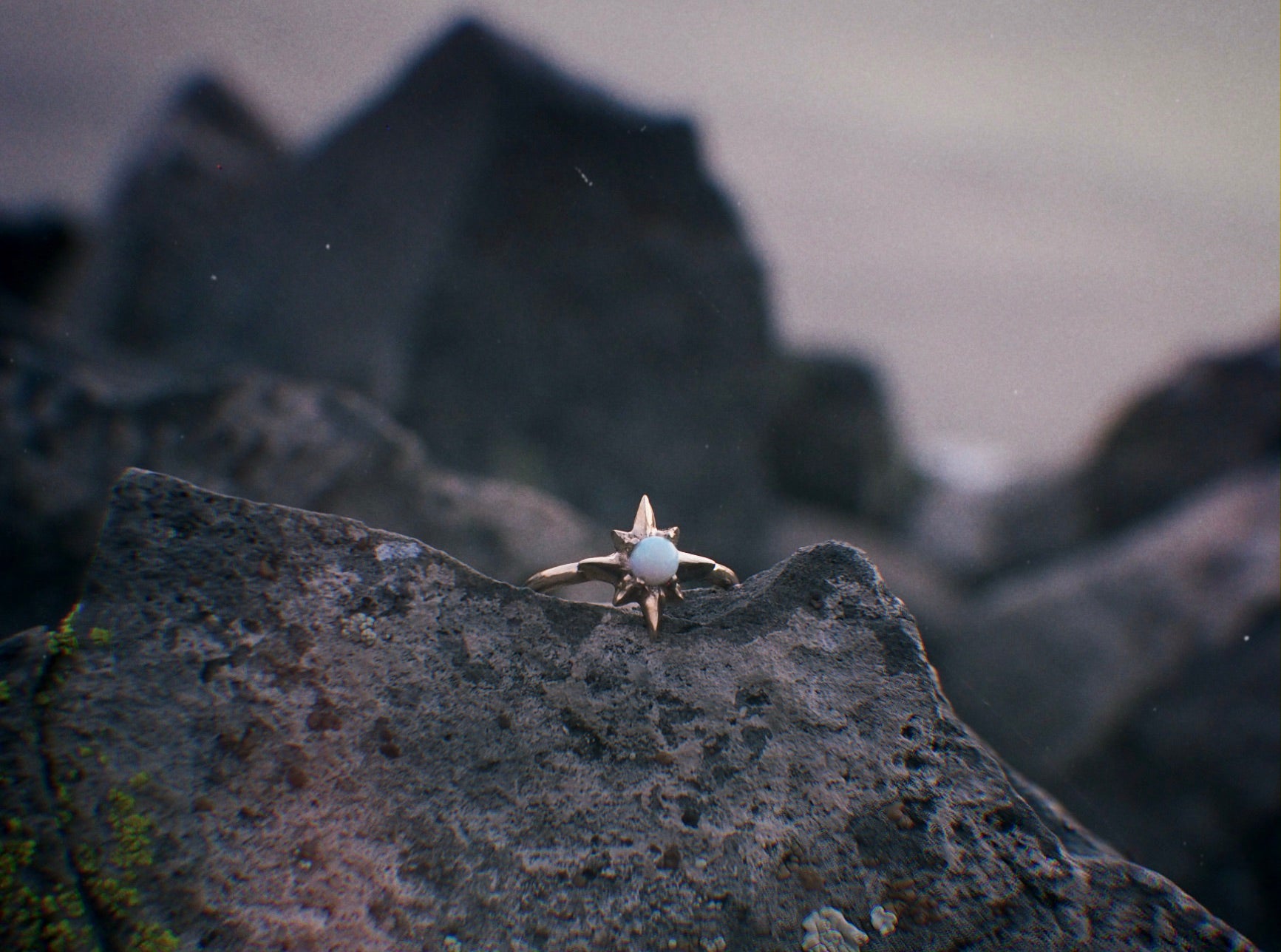 Iron Oxide Designs Polaris star ring set with a lab grown opal amidst a rocky coastal background