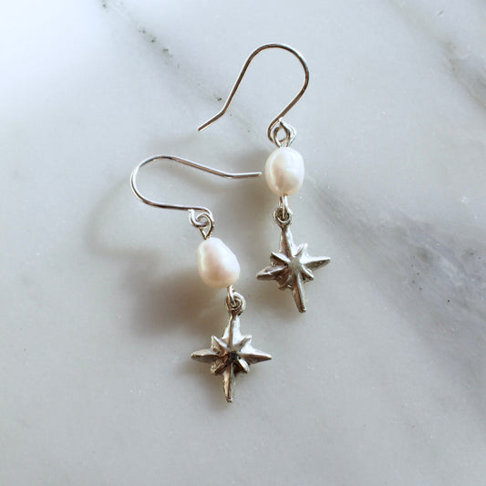 Dainty pearl and star earrings, featuring a 7mm oval shaped pearl with a tiny silver star hanging below it. 