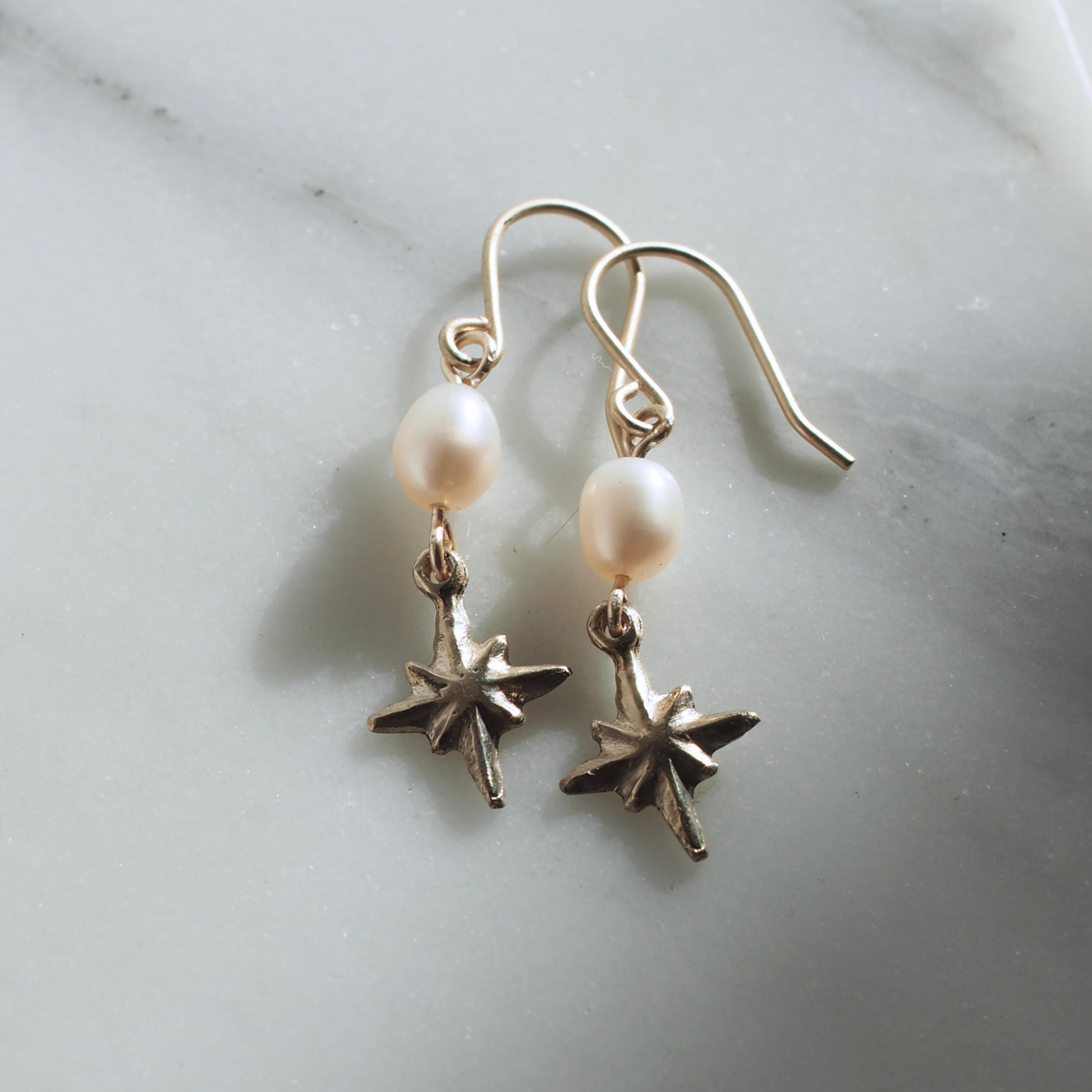 Celestial pearl earrings, featuring a 7mm oval shaped pearl with a tiny silver or bronze star hanging below it. 
