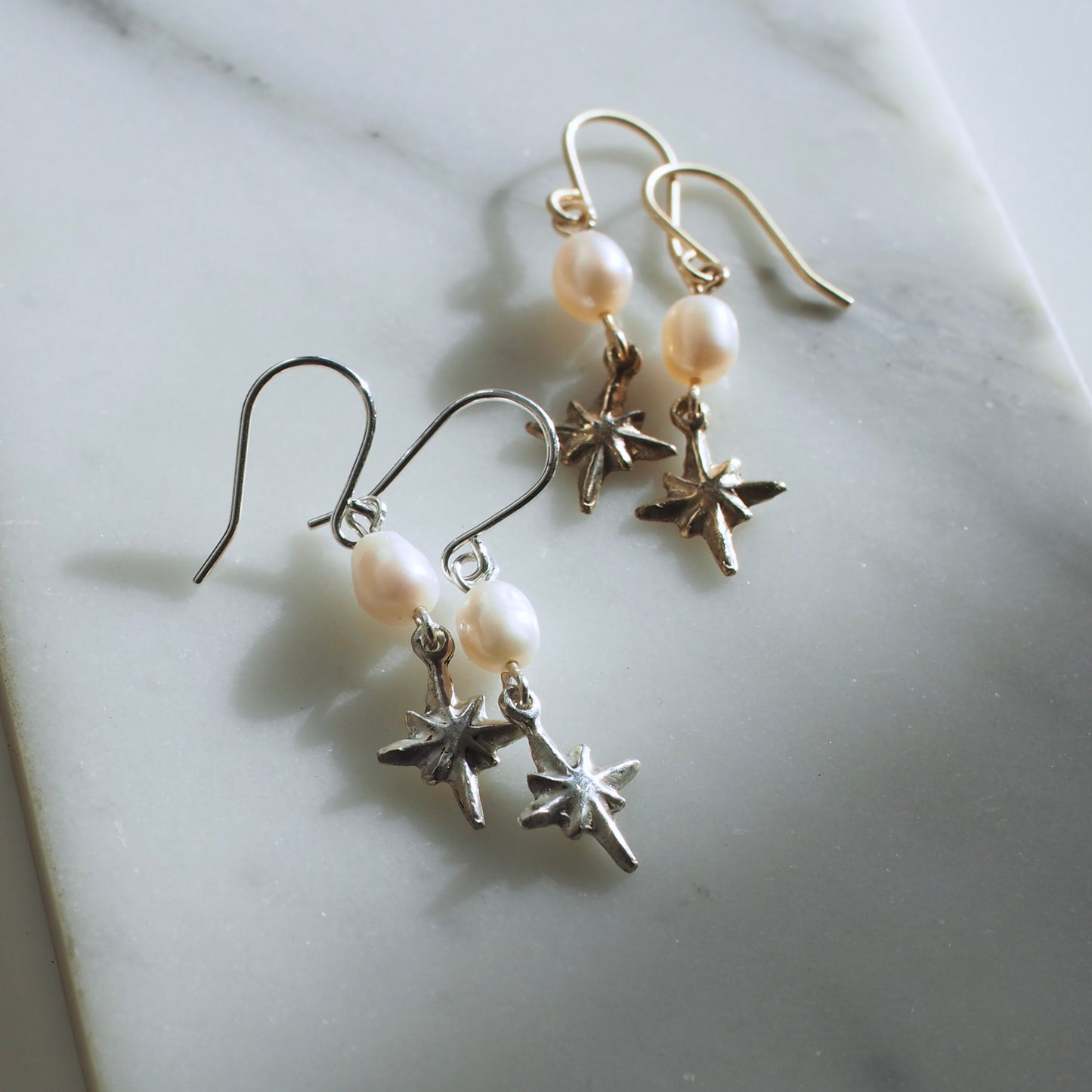 Dainty pearl and star earrings, featuring a 7mm oval shaped pearl with a tiny silver or bronze star hanging below it. 