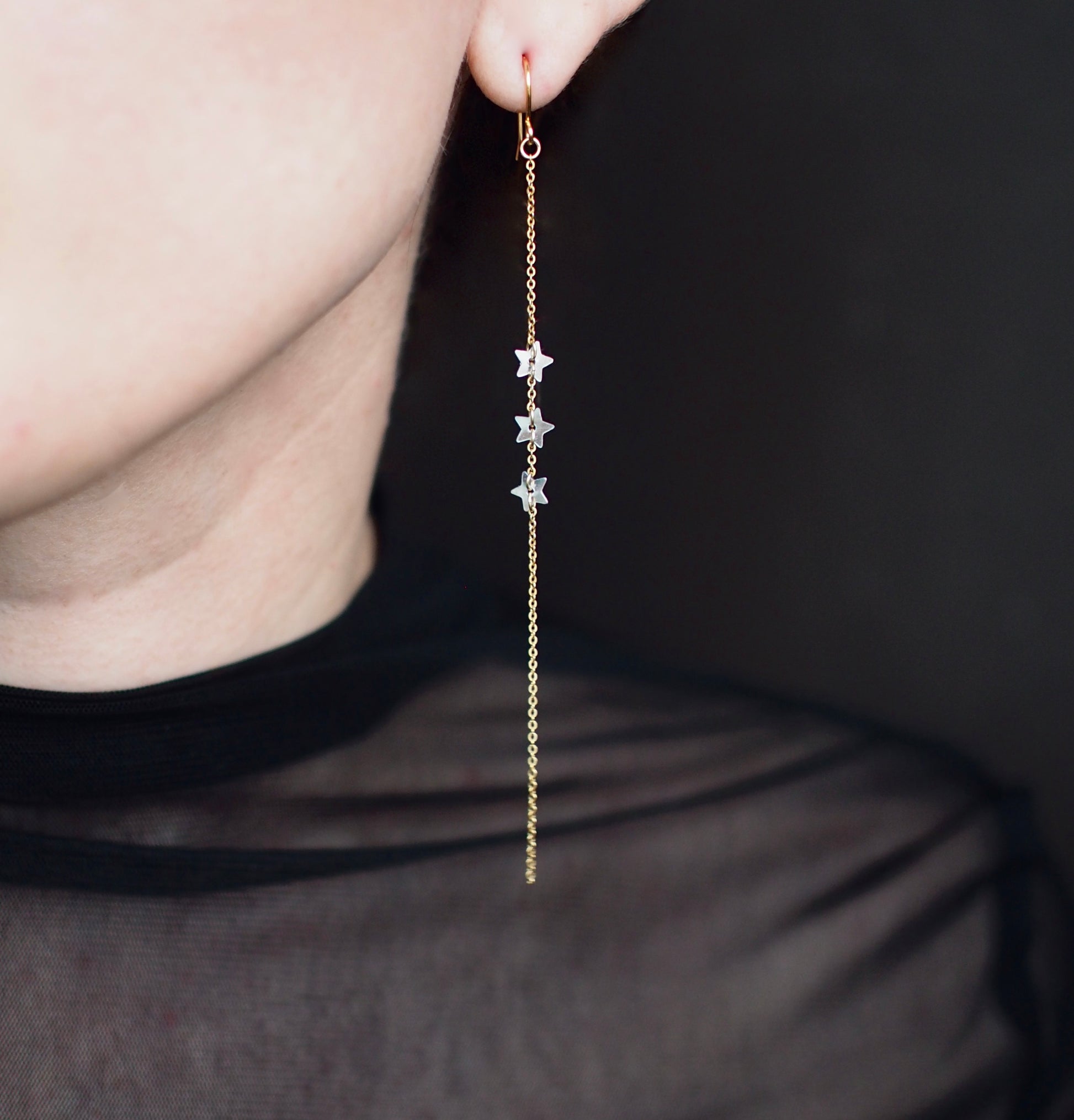 A close-up view of someone wearing handmade dangle  earrings featuring three star shaped silver sequins set on a fine, 5" gold filled chain.