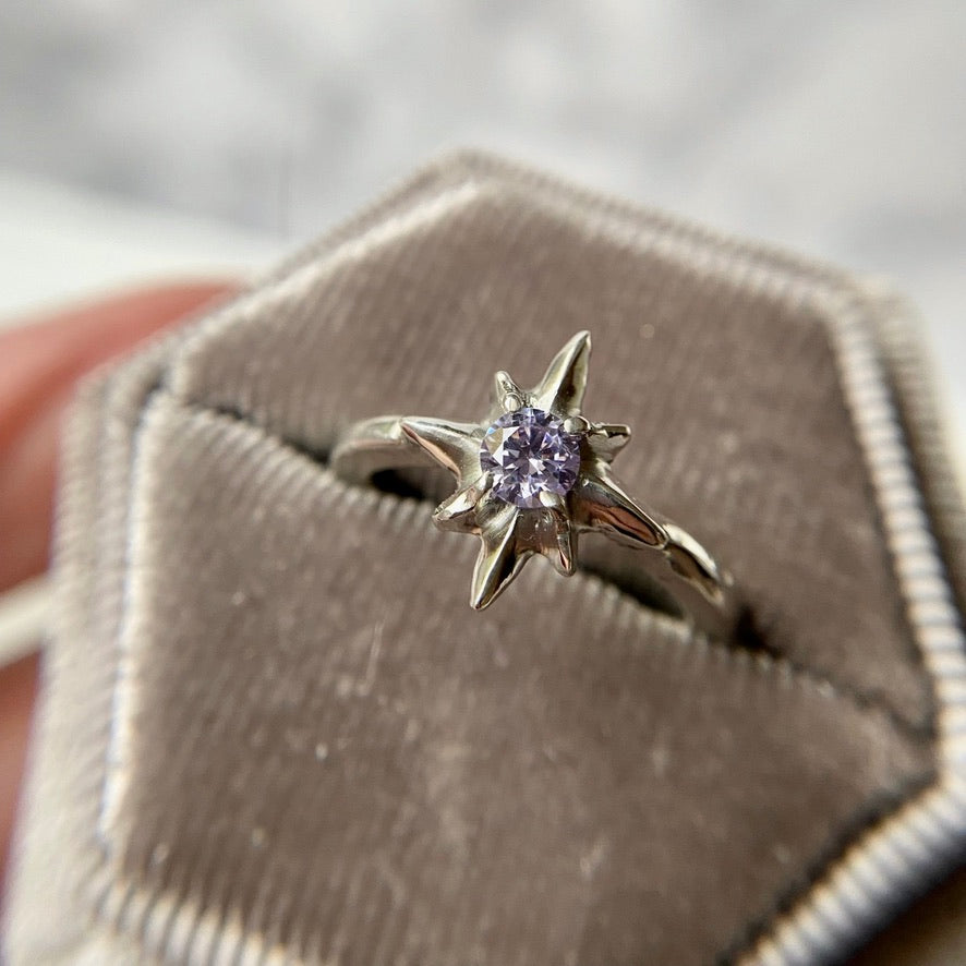 Silver polaris north star ring set with faceted lavender Cubic Zirconia, held in a velvet ring box, handmade by Iron Oxide Designs