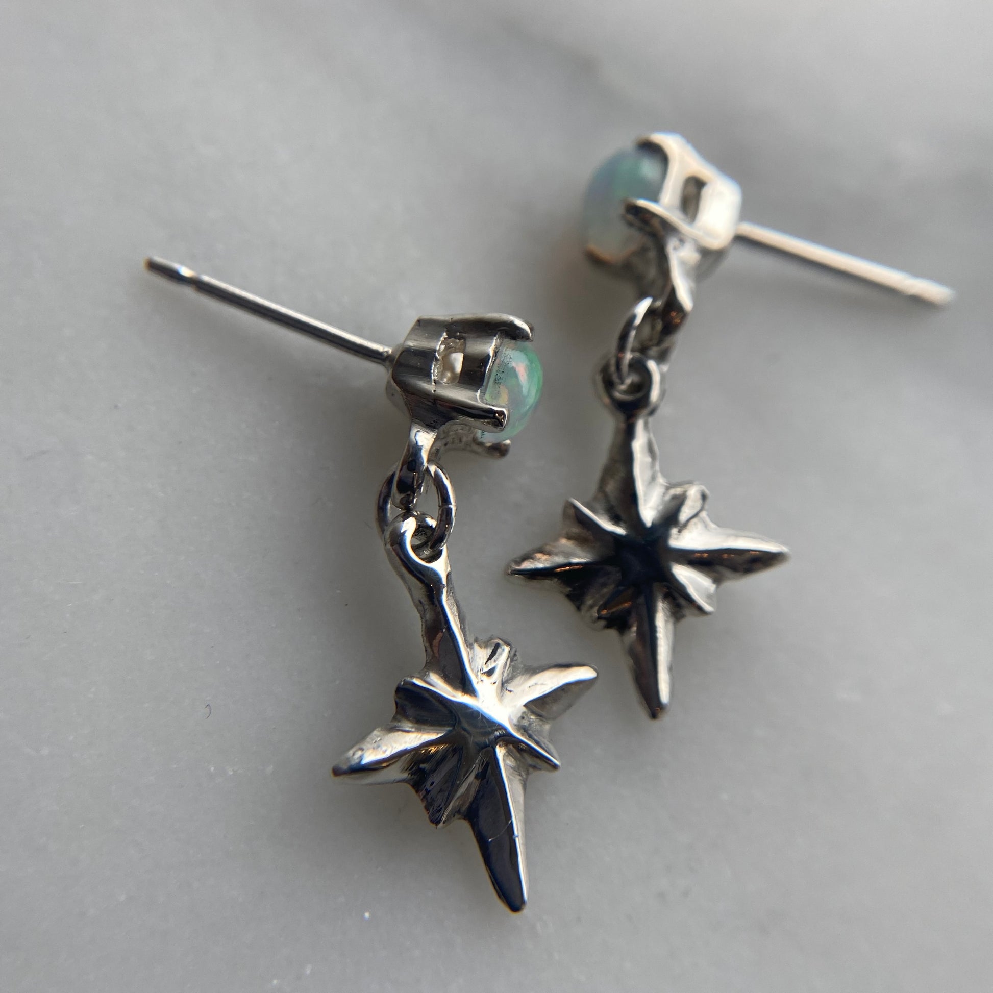 Tiny dangly star earrings set with 4mm clear cubic zirconia, in sterling silver. Made by Iron Oxide Designs, close up showing post back earrings.