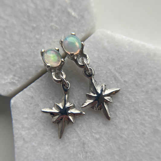 Tiny dangly star earrings set with 4mm sustainably sourced opals, in sterling silver. Made by Iron Oxide Designs