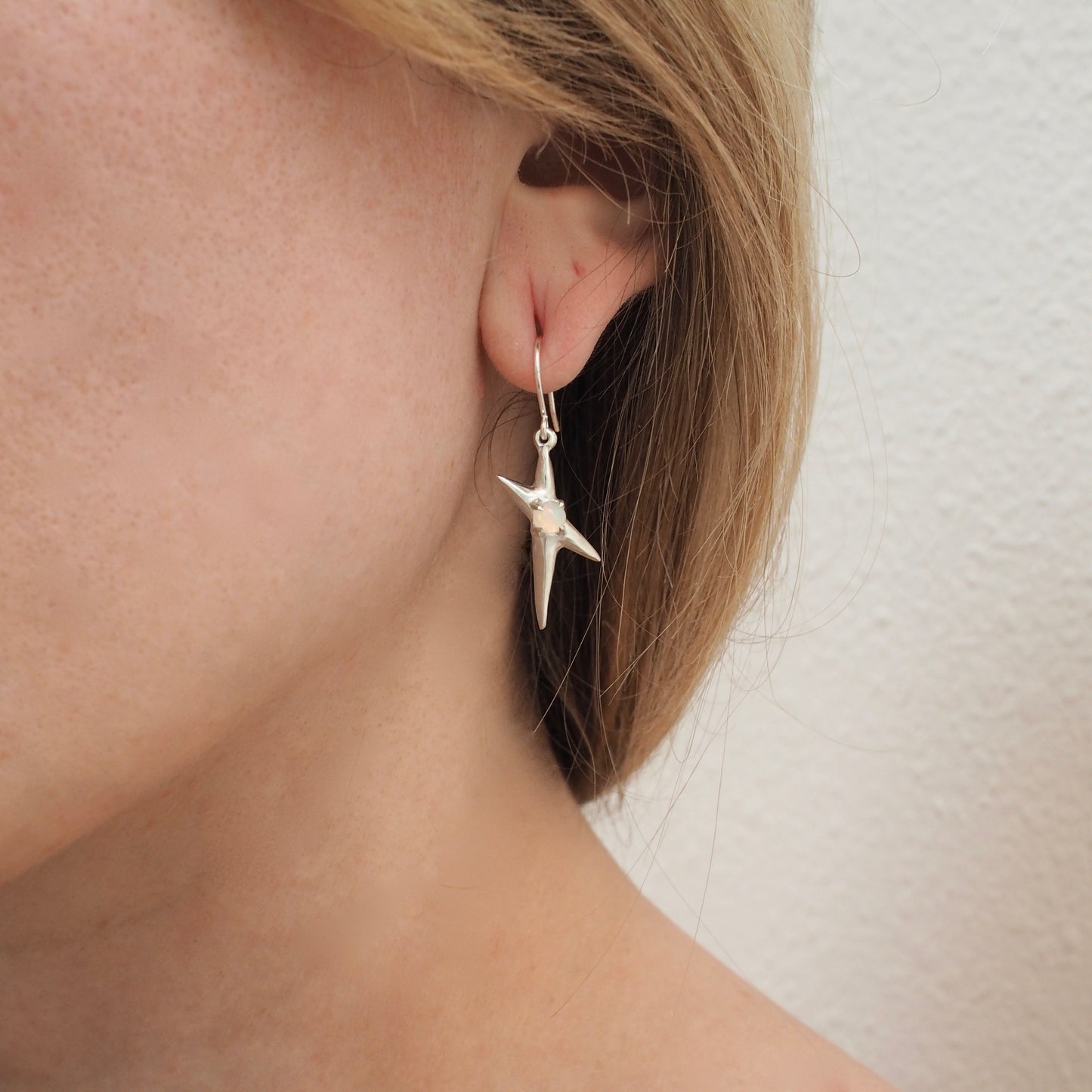 Spikey electric spark earrings set with sustainably sourced opal in sterling silver, shown on a model for scale