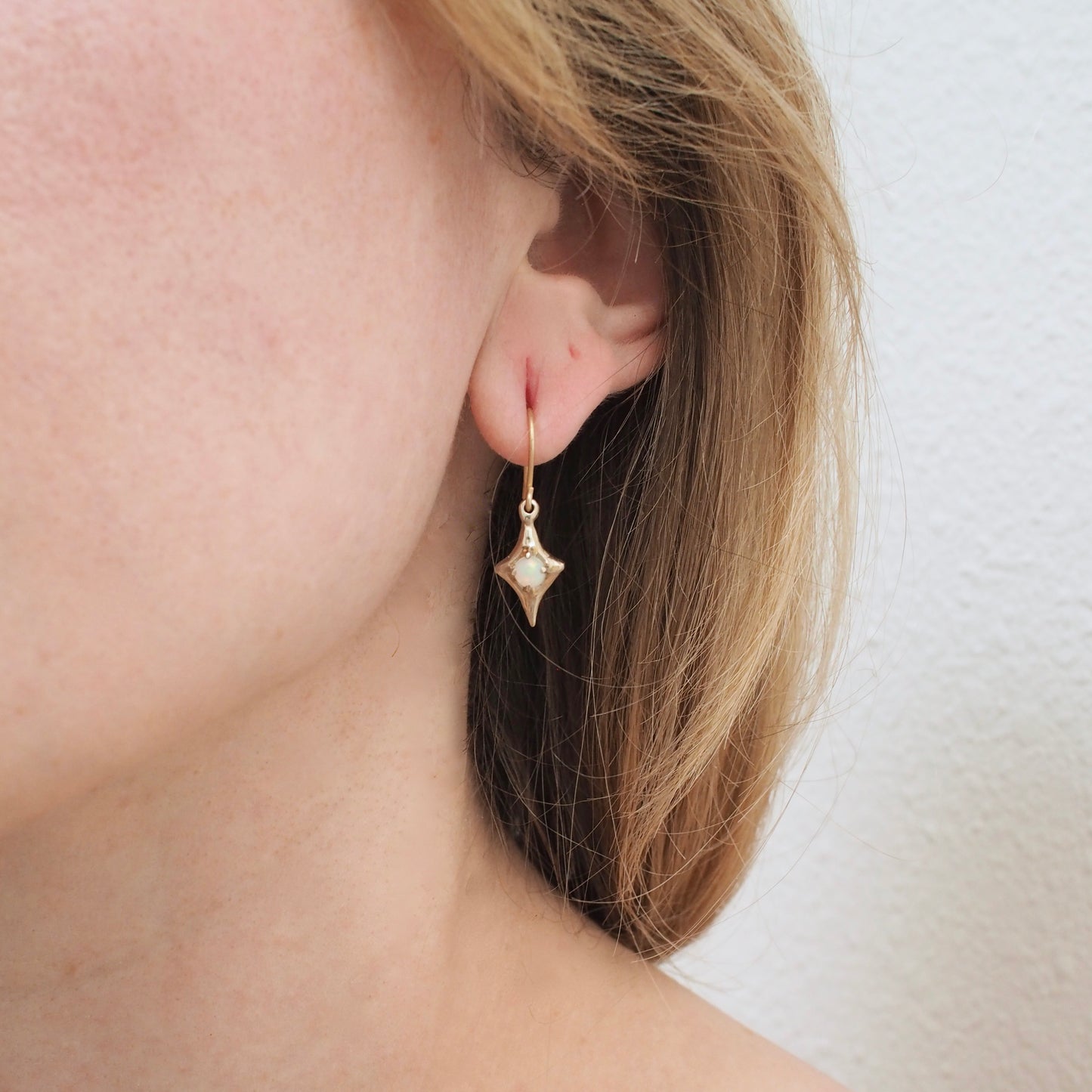 Four point star earrings from Iron Oxide designs set with 4mm natural opals on a model's ear