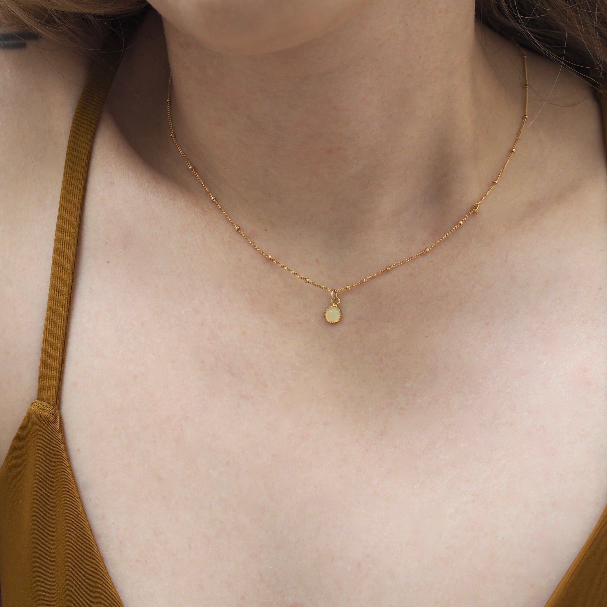 Dainty opal chokers on a dotted gold fill chain shown on a model for scale.