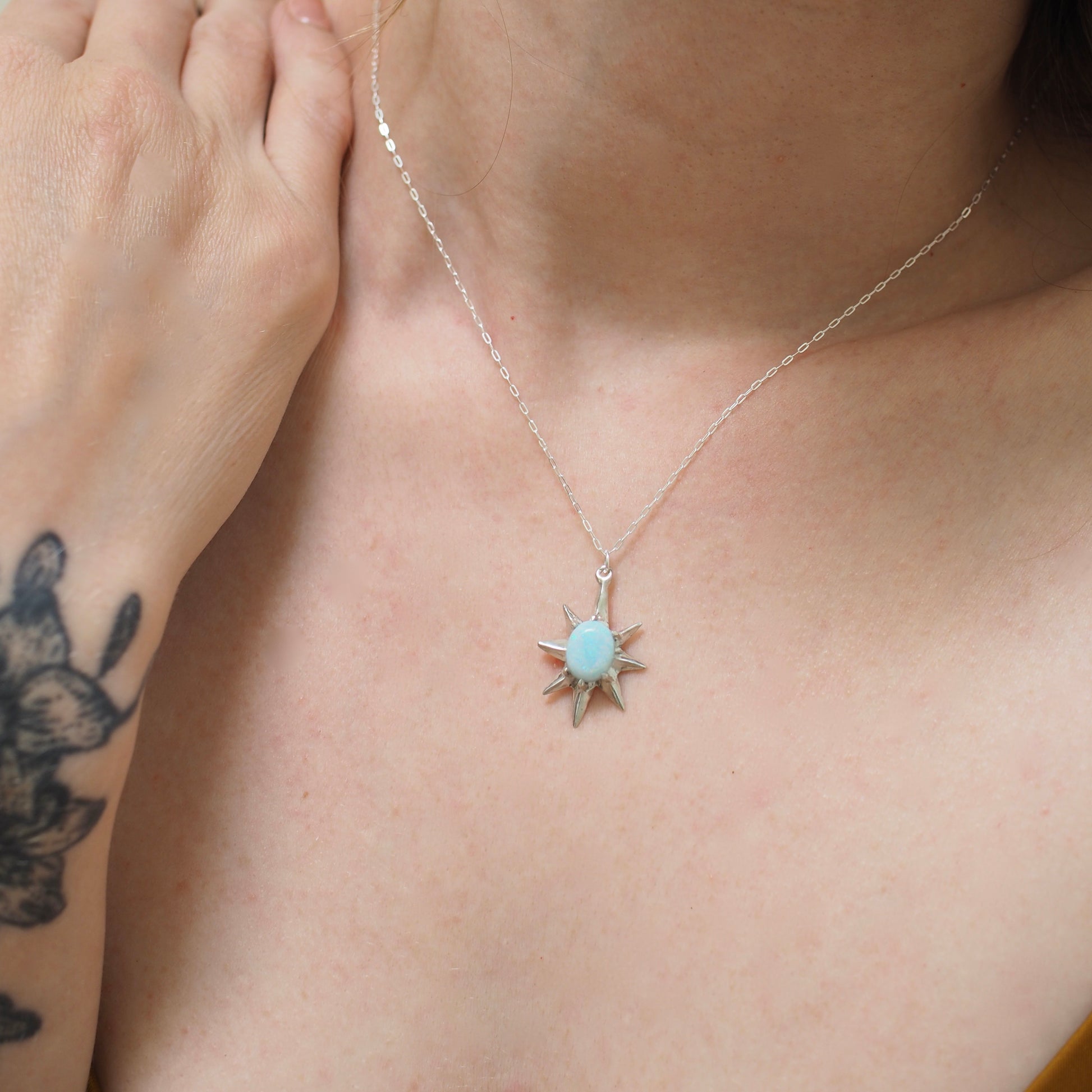 Close up of Supernova large star necklace set with lab grown opal by Iron Oxide Designs shown on a model for scale