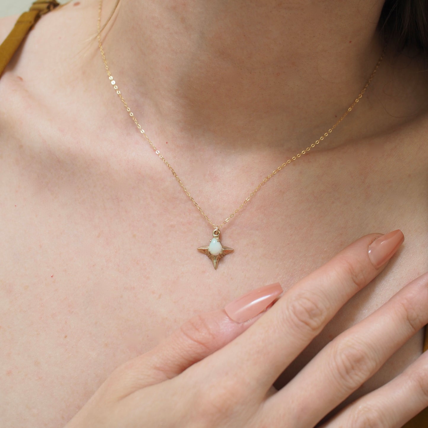 Teardrop shaped lab grown opal set in a four point star in gold tone bronze and sterling silver handmade by Iron Oxide Designs, shown on a model for scale