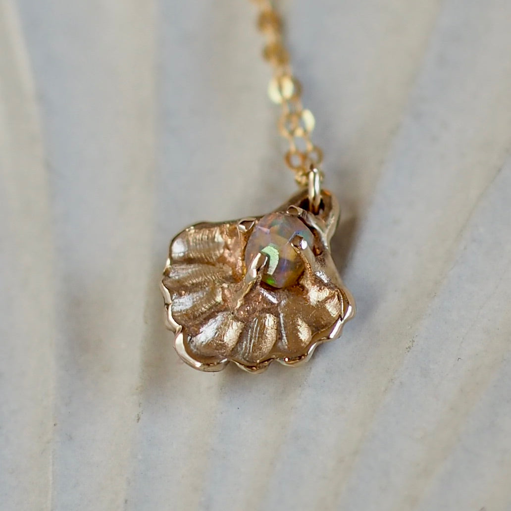 Close up of a gold tone Seashell necklace containing a tiny opal in place of a pearl, handmade by Iron Oxide Designs