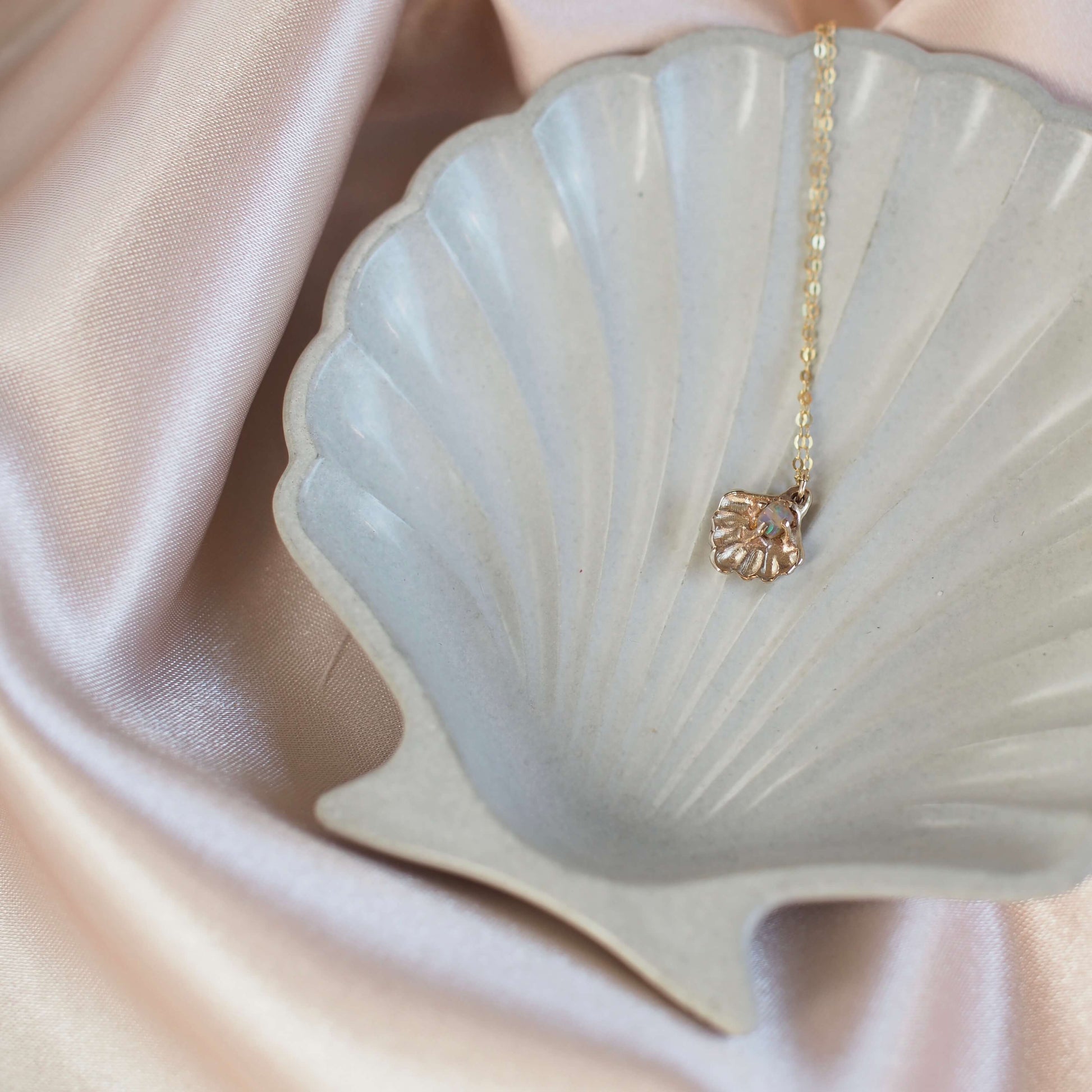 Close up of a gold tone Seashell necklace containing a tiny opal in place of a pearl, handmade by Iron Oxide Designs on a shell jewelry plate