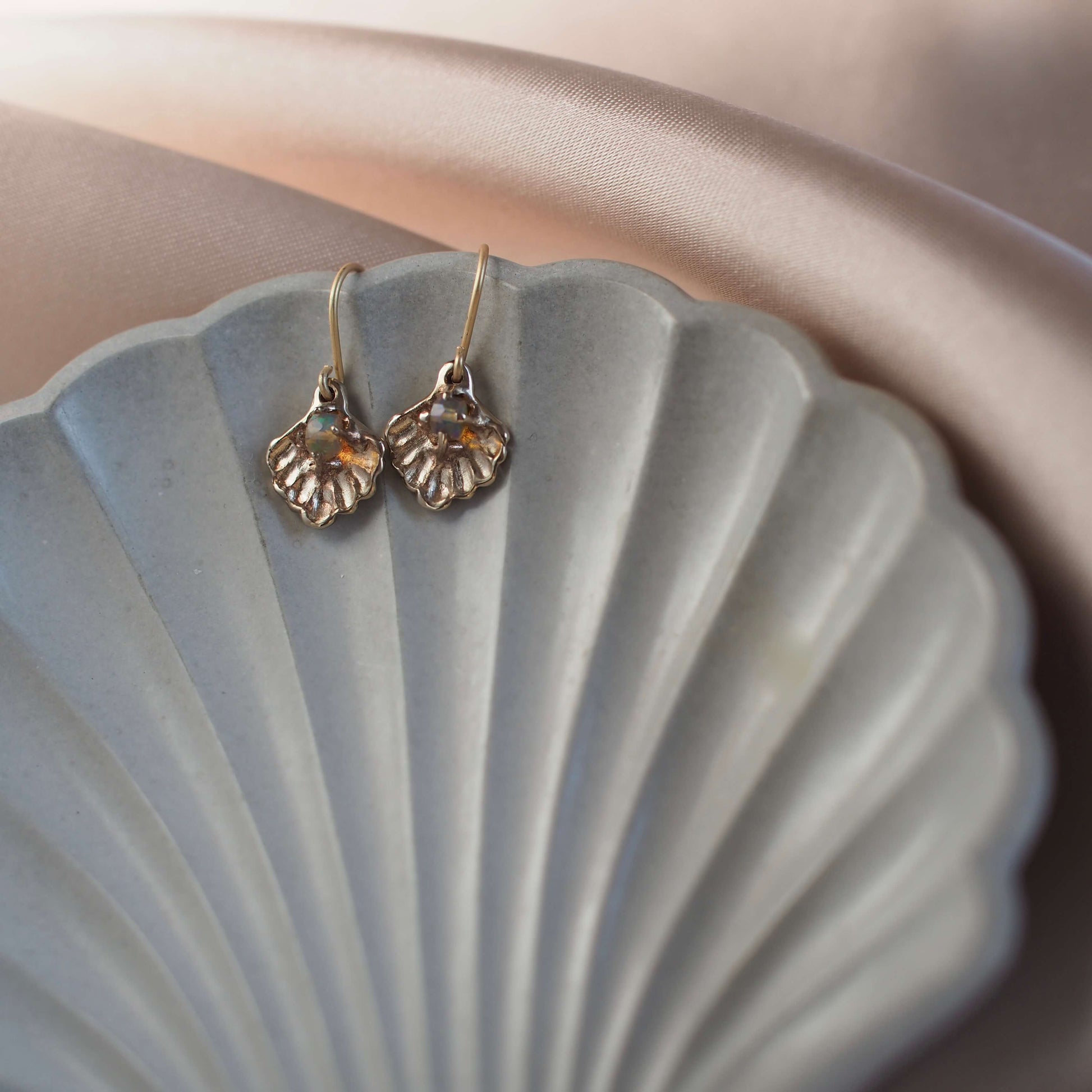 Oyster shell earrings containing a small opal "pearl", cast in gold tone bronze by Iron Oxide Designs set on a shell backdrop