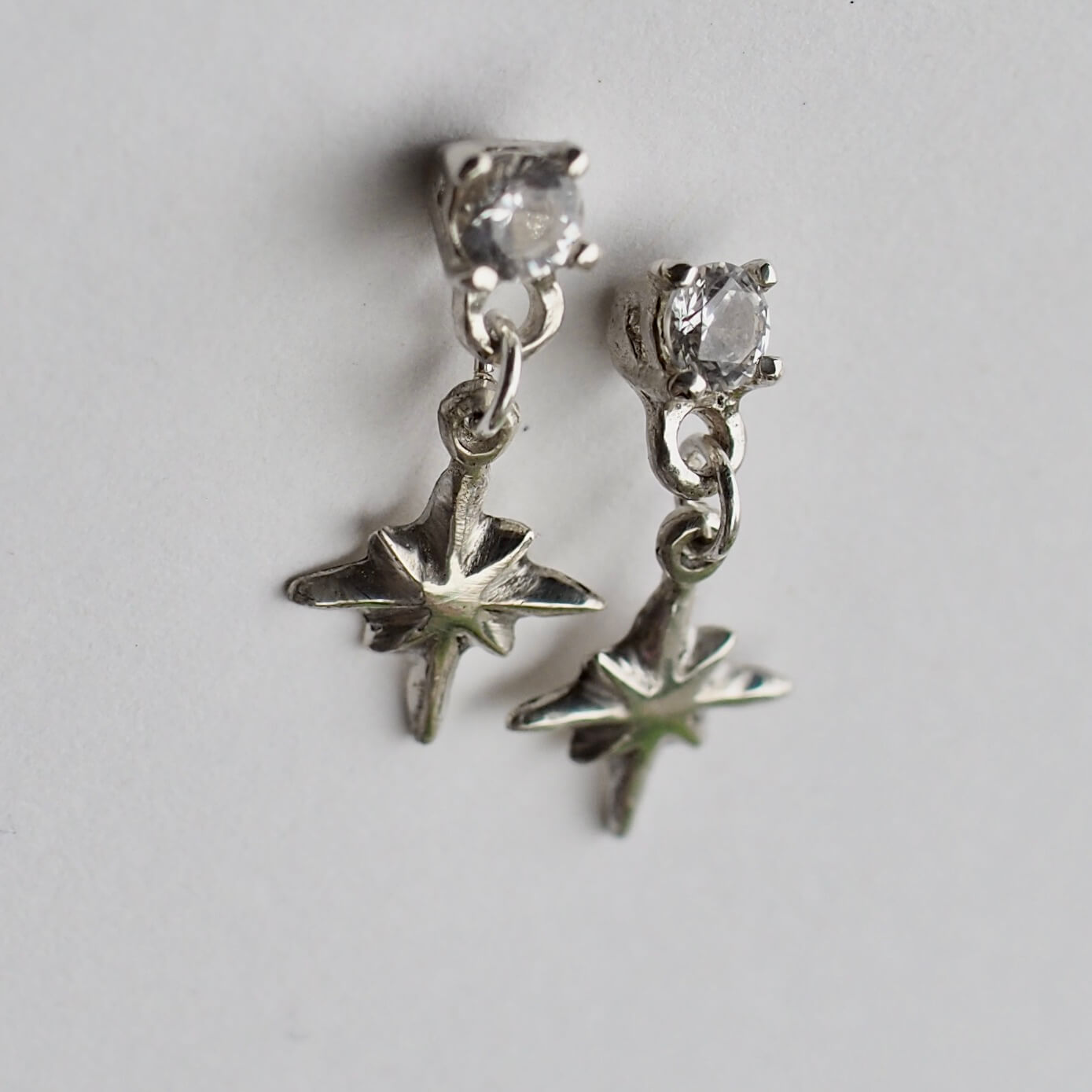 Tiny dangly star earrings set with 4mm clear cubic zirconia, in sterling silver. Made by Iron Oxide Designs