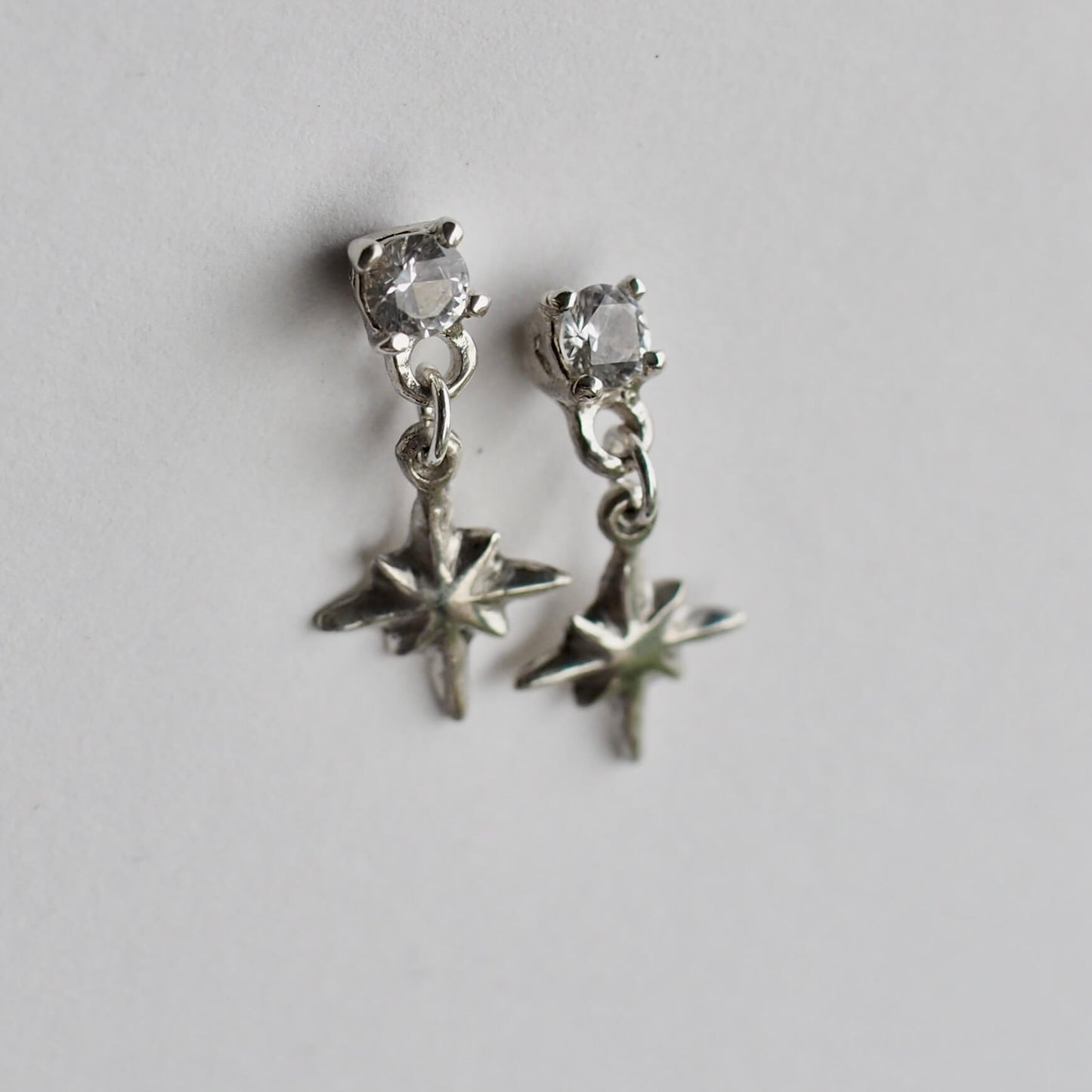 Tiny dangly star earrings set with 4mm clear cubic zirconia, in sterling silver. Made by Iron Oxide Designs