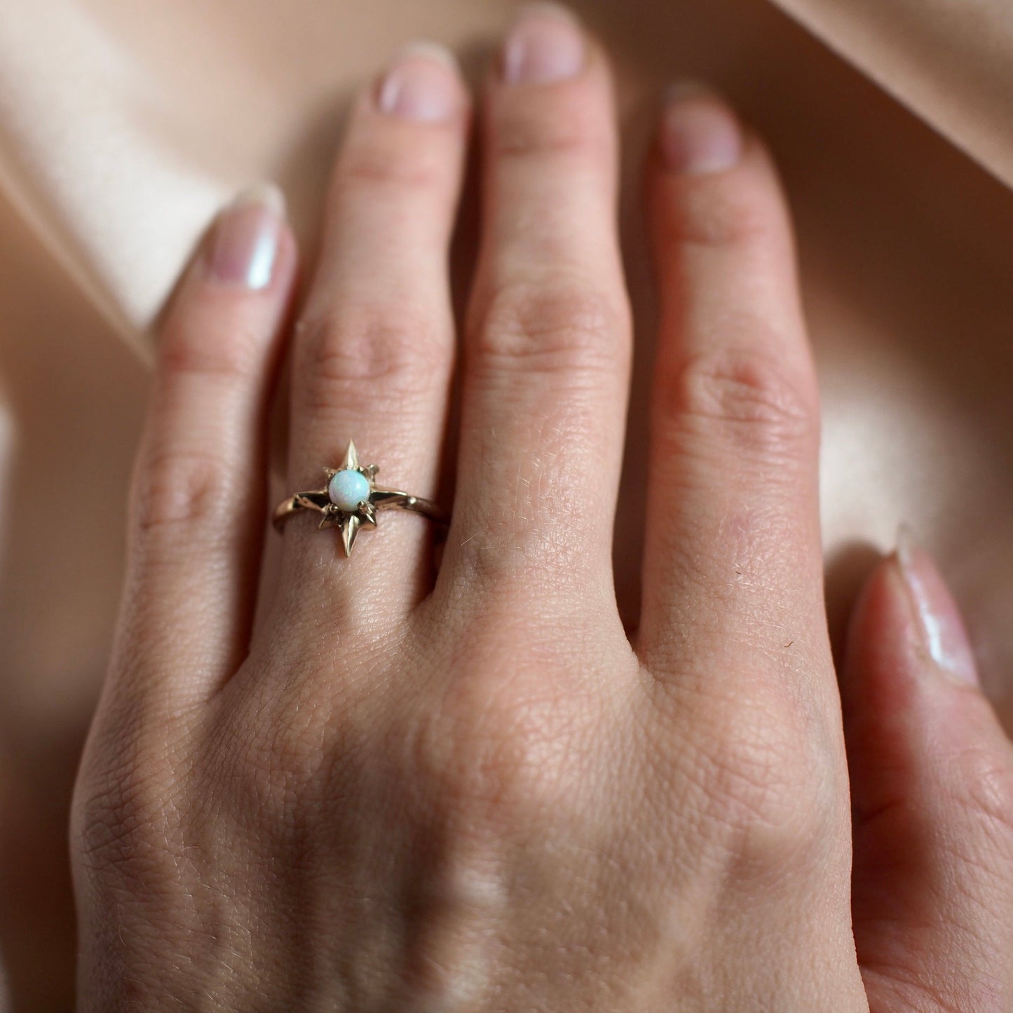 Polaris north star ring set with a tiny lab grown opal in gold tone bronze worn by a model, handmade by Iron Oxide Designs