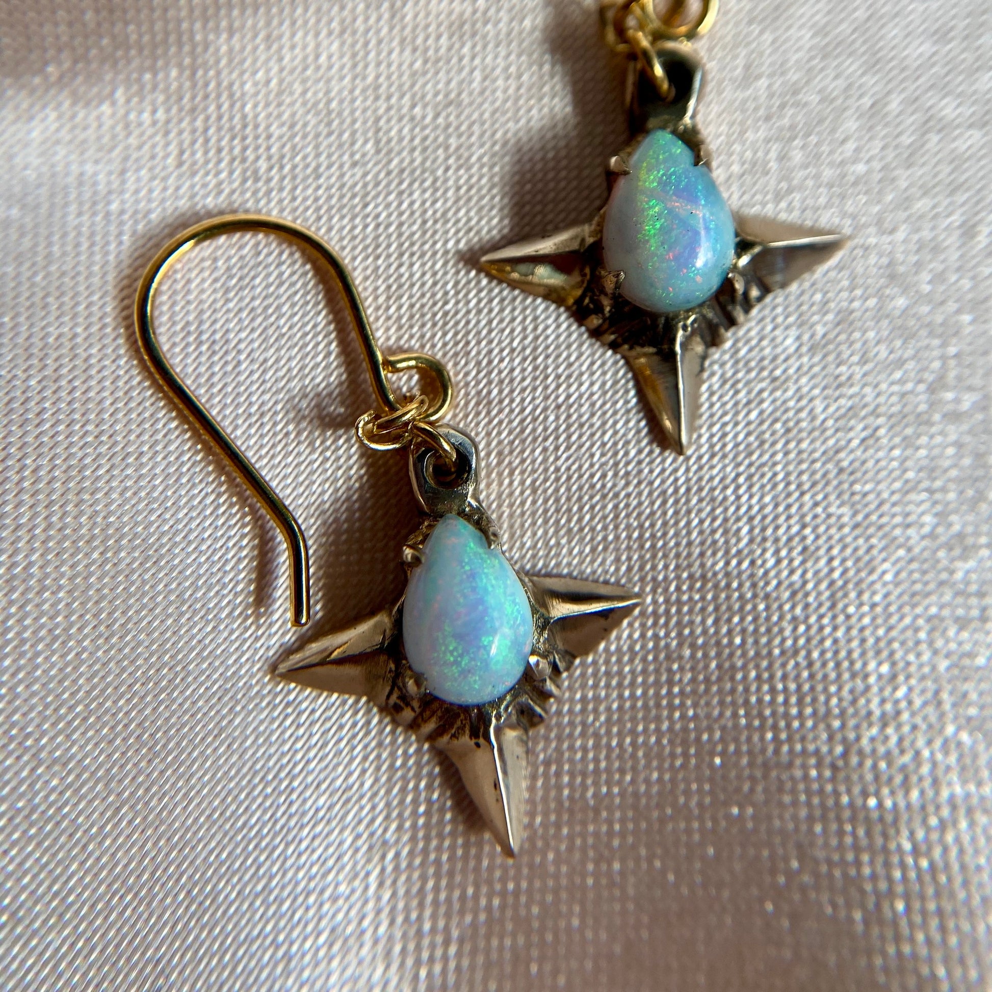 Close up of Teardrop shaped lab grown opal set in 4 point star setting in gold tone bronze handmade by Iron Oxide Designs