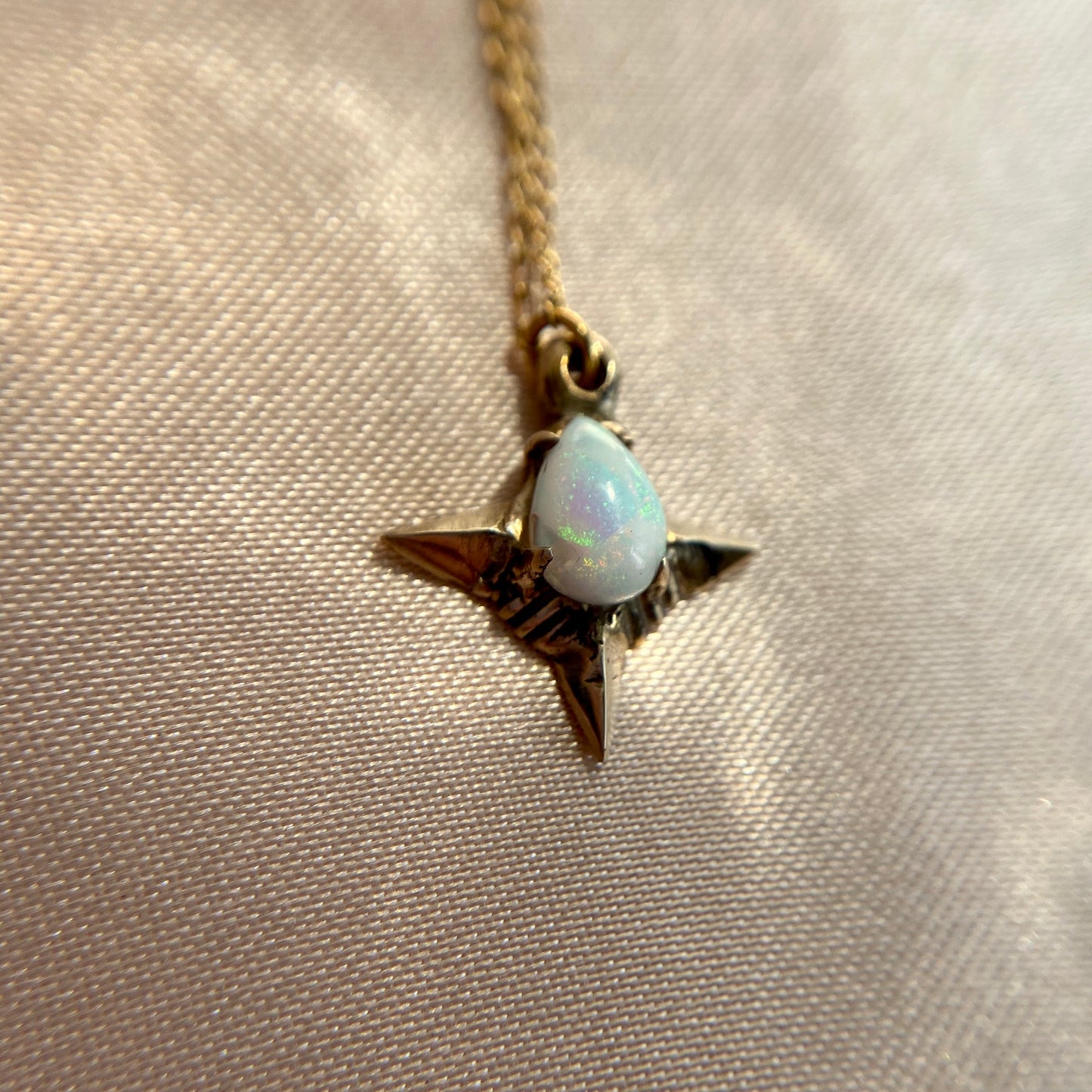 Close up of Teardrop shaped lab grown opal set in a four point star in gold tone bronze handmade by Iron Oxide Designs