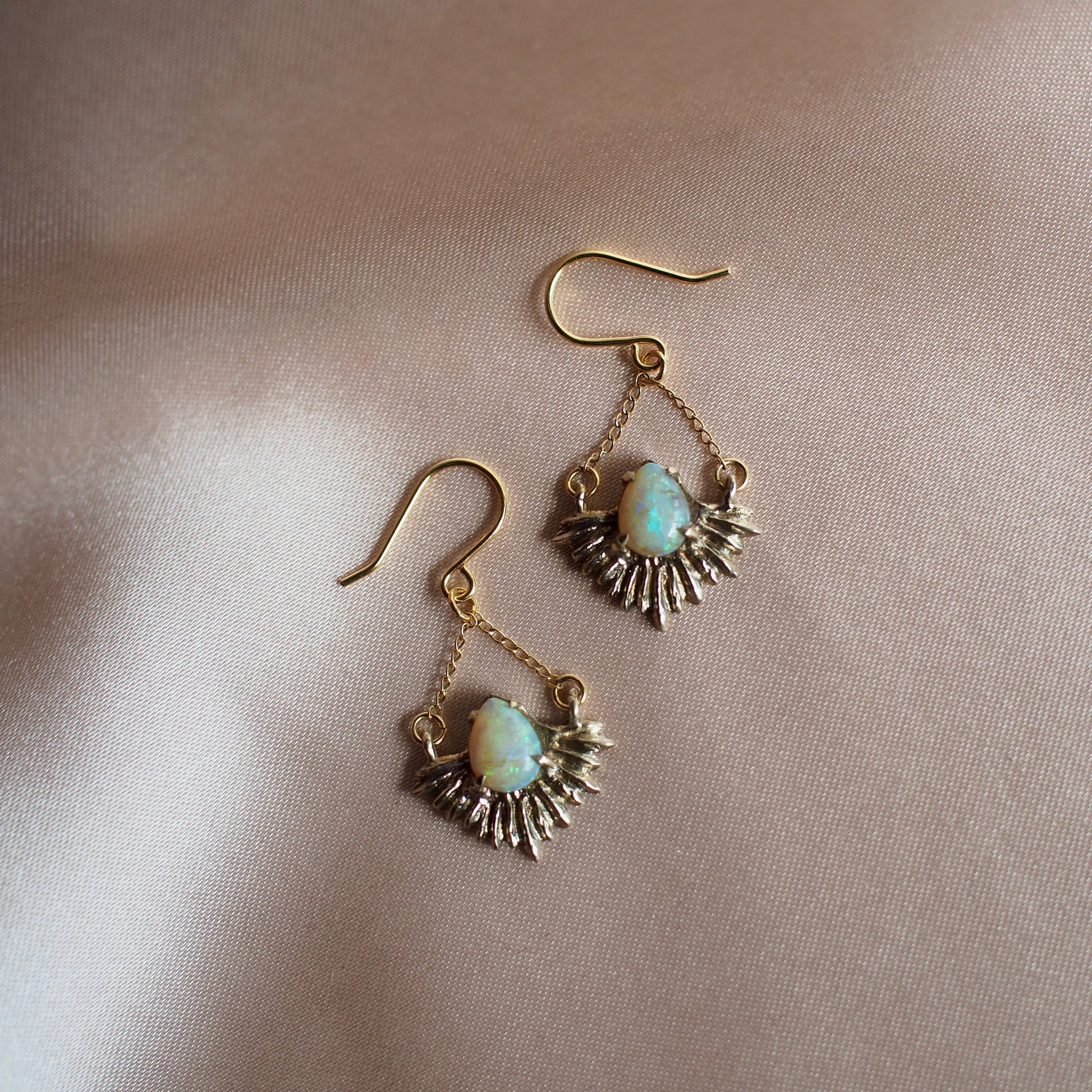 Gold Tone bronze earrings in the shape of beams of light set with teardrop shaped, lab grown opals.